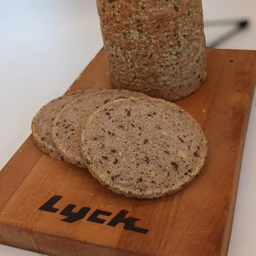 Ein angeschnittenes Kastenbrot mit Saaten, davor drei Scheiben auf einem Lyck-Brett.
