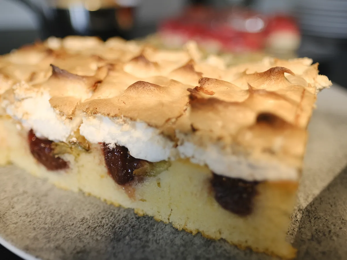 Ein Stück Blechkuchen mit Kirschen unter einer Baiserhaube.
